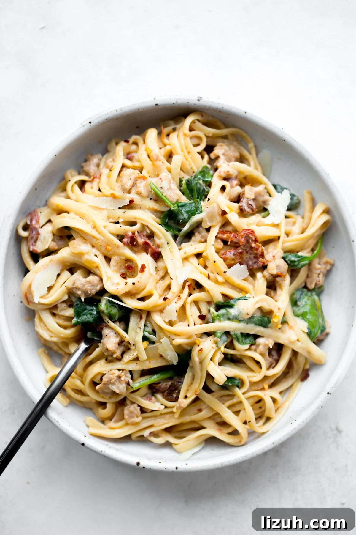 bowl of instant pot pasta with sausage spinach and sun-dried tomatoes on a white background
