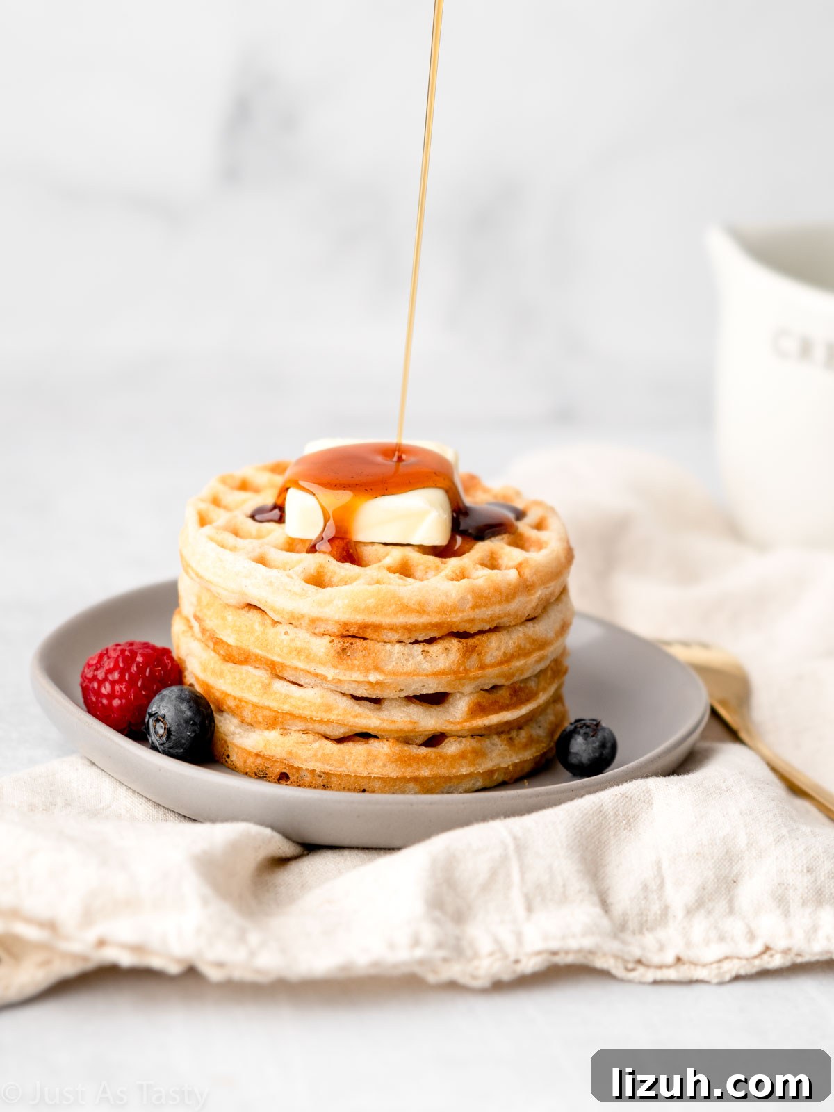 Syrup being poured onto stack of waffles. 