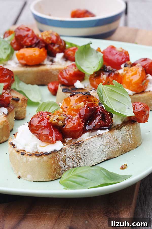 Slow-Roasted Tomato and Ricotta Bruschetta Recipe 2 A closeup of a piece of toast with ricotta, tomatoes and basil on it on a white plate.