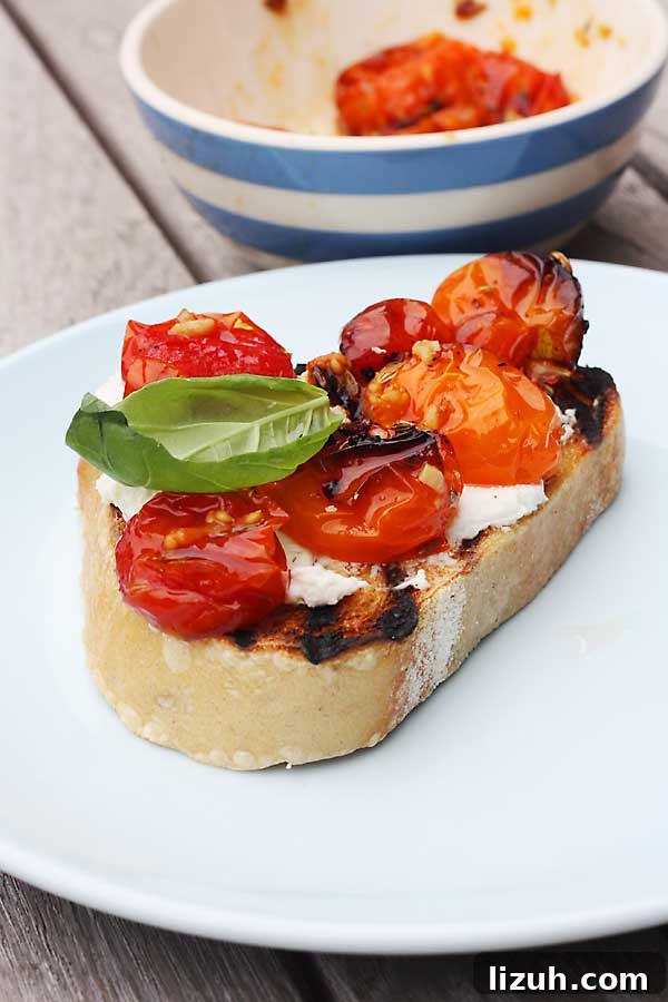 Slow-Roasted Tomato and Ricotta Bruschetta Recipe 8 A closeup of ricotta and roasted tomatoes and basil on a piece of toast on a white plate.