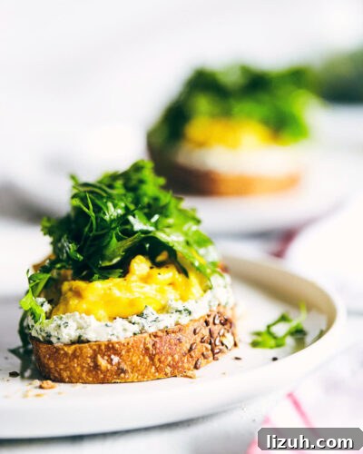 Herbed Goat Cheese Toast with Fluffy Scrambled Eggs 7 Side view of scrambled goat cheese toast on a plate with a second plate in the background