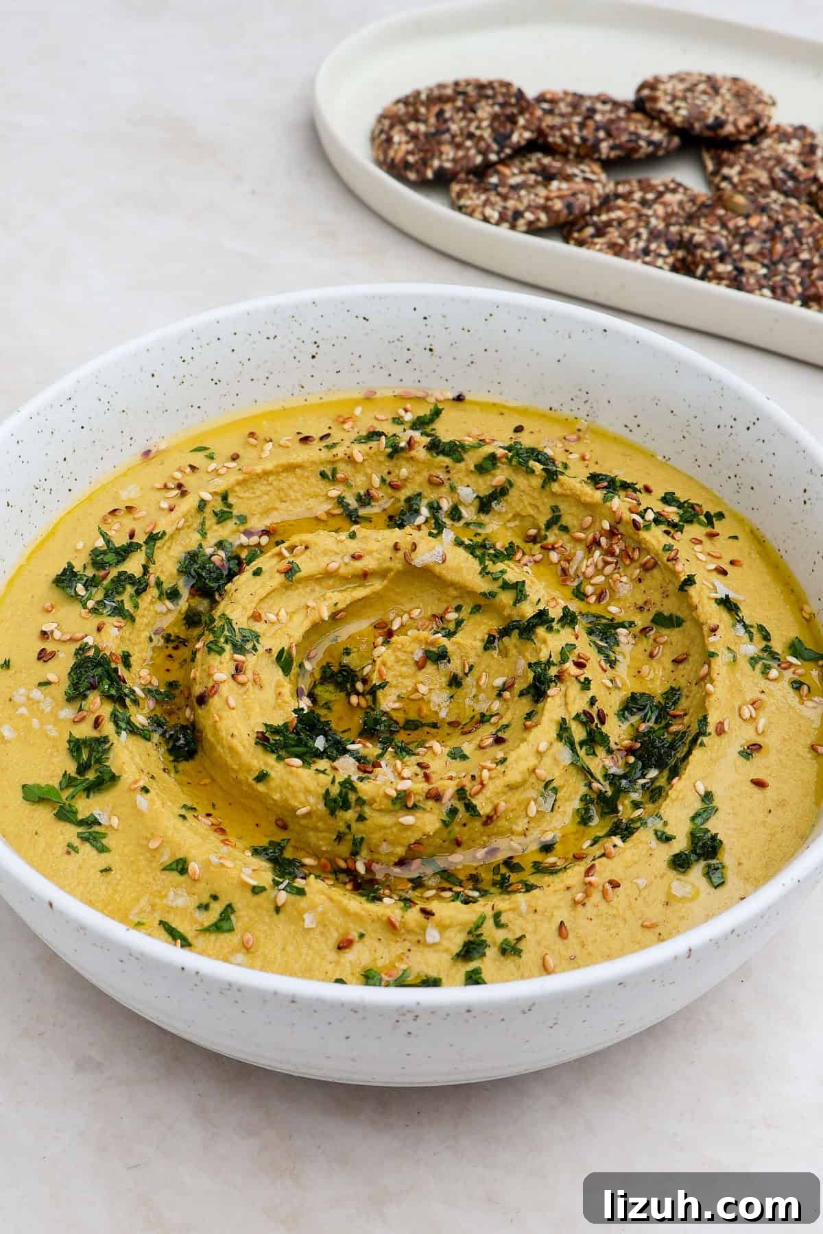 Side shot of the golden lentil hummus with crackers in the background.