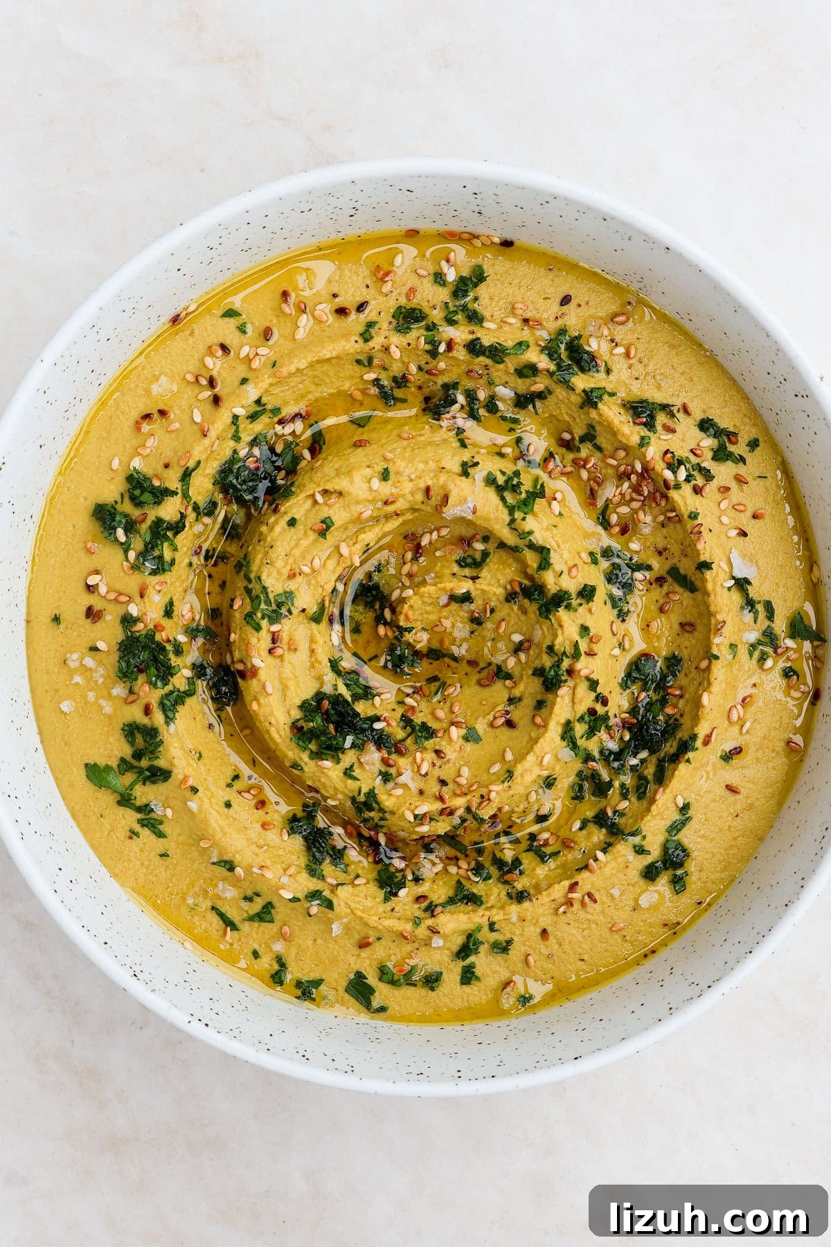 Hummus served in a bowl with herbs, sesame seeds and olive oil.