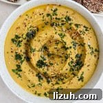 Lentil hummus in a bowl with chopped herbs and sesame seeds on top.