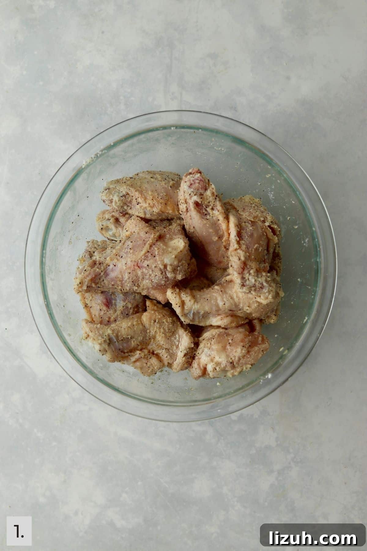 Crispy Garlic Parmesan Air Fryer Chicken Wings 4 chicken wings tossed in spices in a glass bowl.