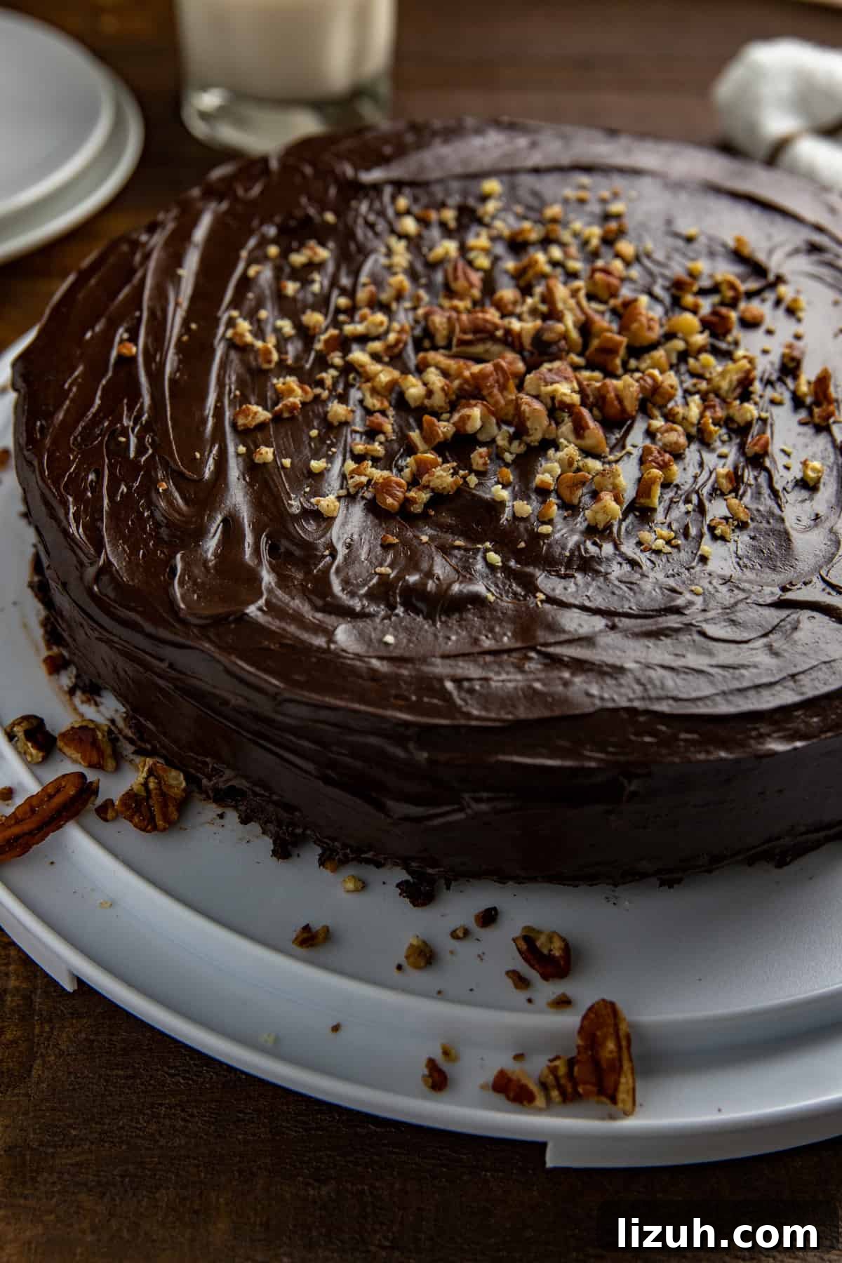 Whole cake on white cake pan with white plates and glass of milk in background.