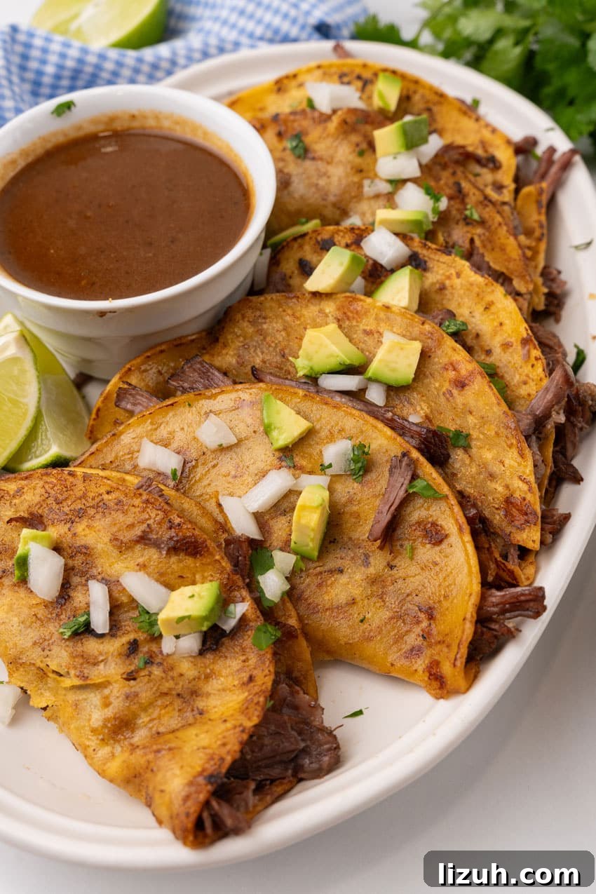 Instant Pot Birria Tacos Recipe — Rich, Juicy Beef Tacos 2 instant pot birria tacos topped with avocado pieces and diced white onion arranged in a row on a white serving platter