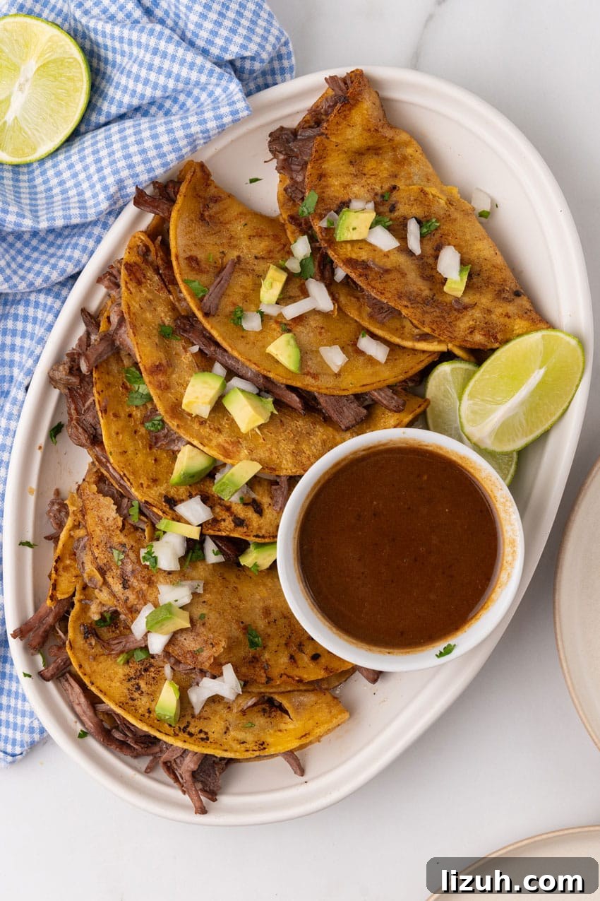 Instant Pot Birria Tacos Recipe — Rich, Juicy Beef Tacos 3 instant pot birria tacos topped with avocado pieces and diced white onion arranged in a row on a white serving platter