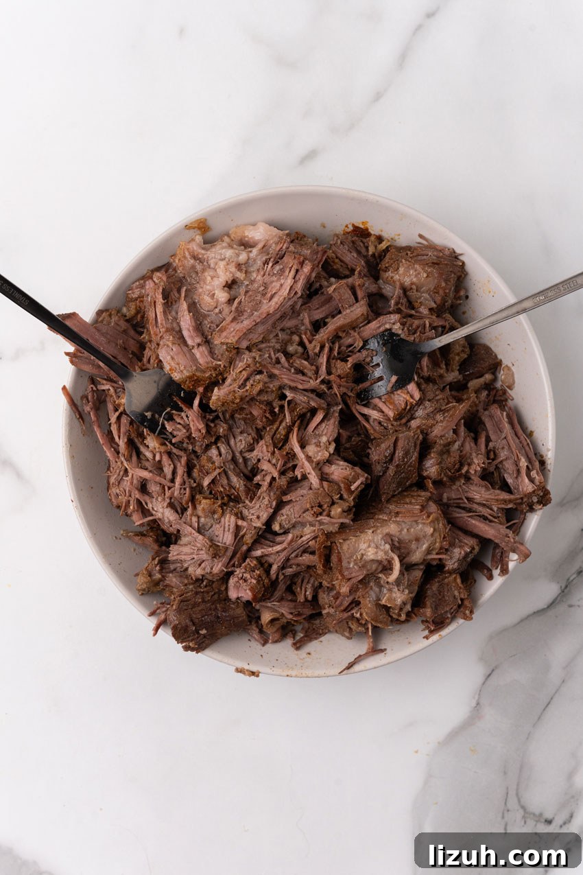 Instant Pot Birria Tacos Recipe — Rich, Juicy Beef Tacos 5 shredded beef on a white plate with two forks resting on the side