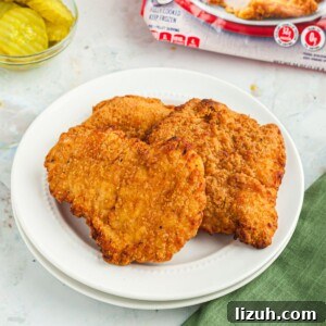 Golden crispy chicken breasts on a white plate in front of pickles and a red bag of chicken