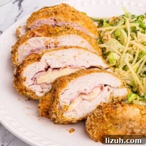 Golden crispy coated chicken sliced and filled with ham and cheese on a white plate