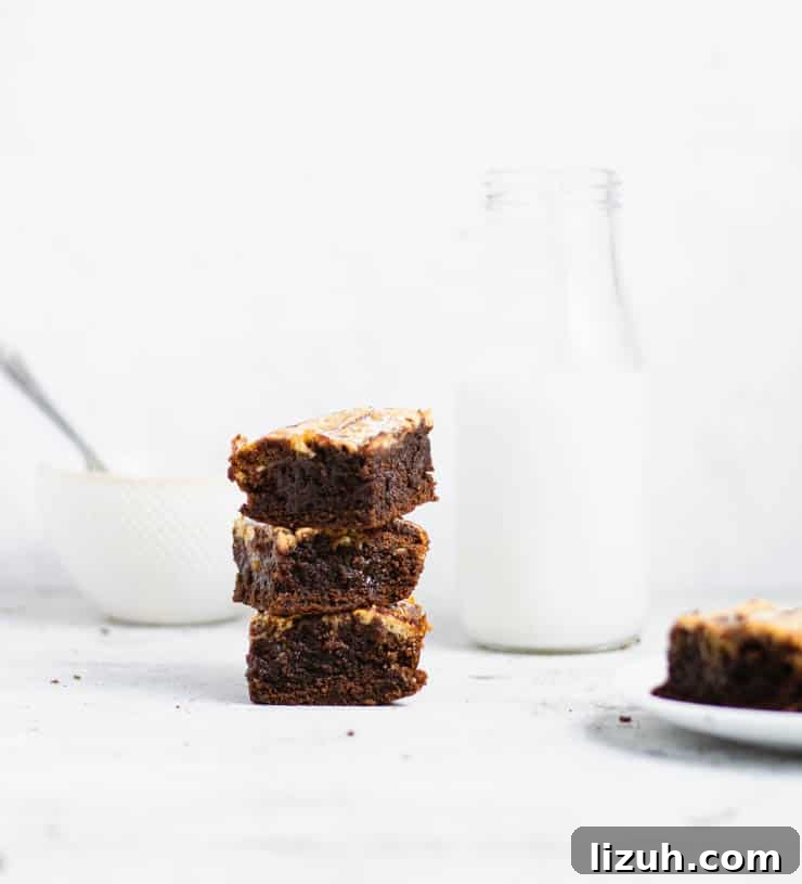 stack of cheesecake brownies next to a glass of milk and a bowl