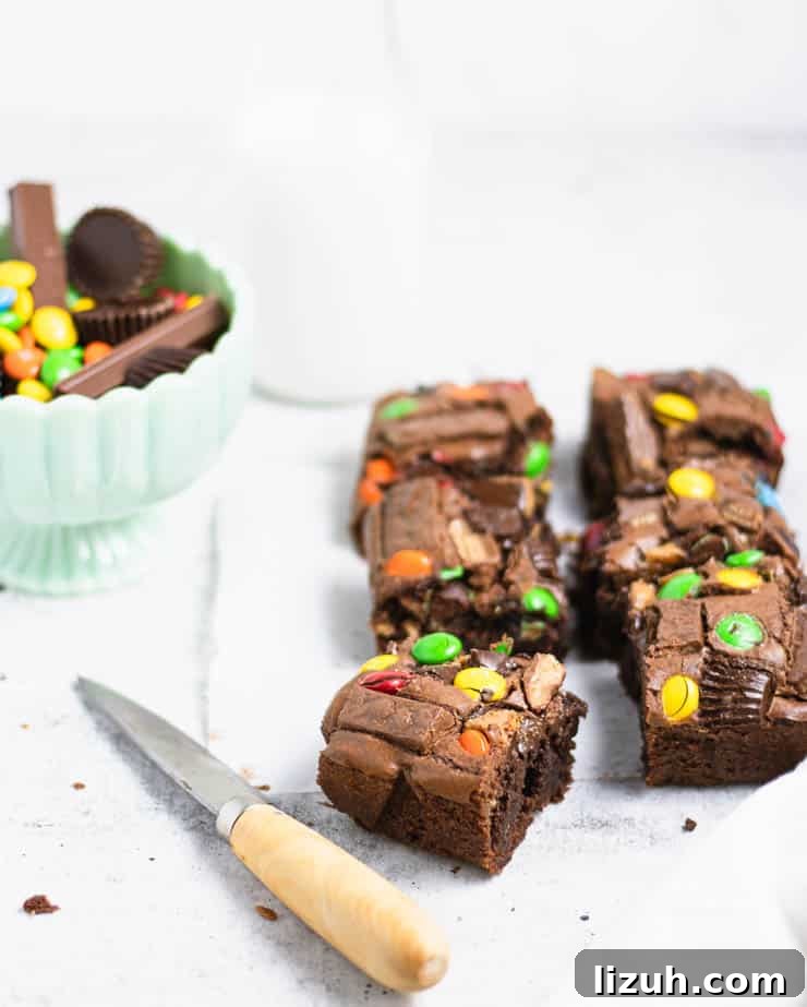 brownies with candy pieces on top next to a bowl of candy and a glass of milk