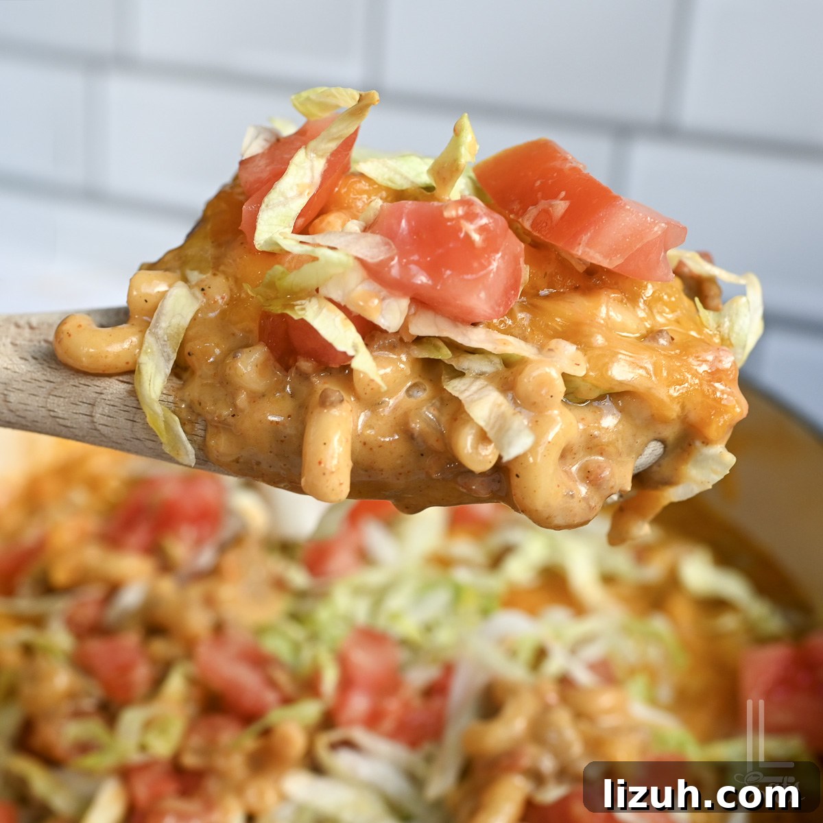 One-Pot Taco Mac and Cheese Recipe for Quick Weeknight Dinners 2 holding taco mac and cheese, topped with lettuce and tomato, in a spoon.