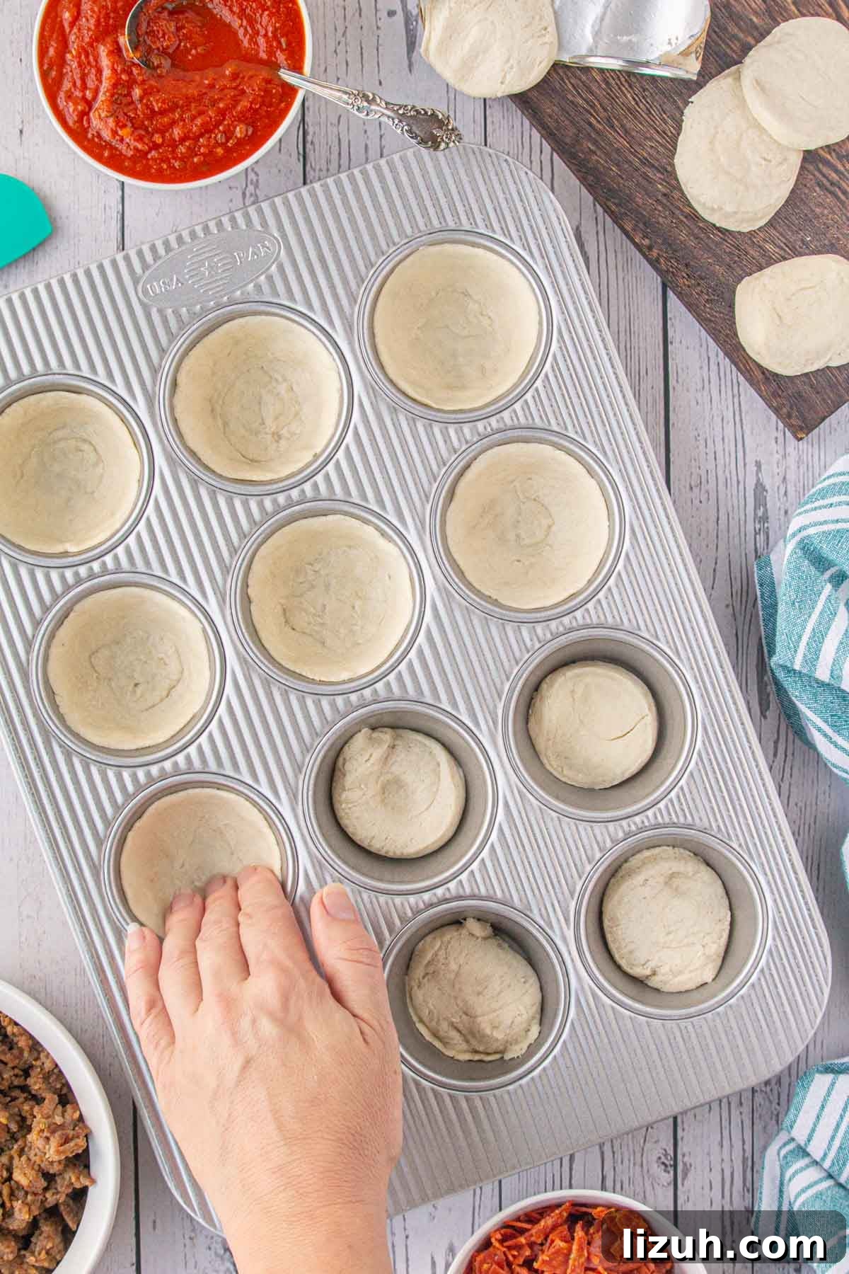 Mini Pizza Cups Recipe: Homemade Pizza Bites in 30 Minutes 4 Pressing the biscuit dough into the wells of a muffin tin.