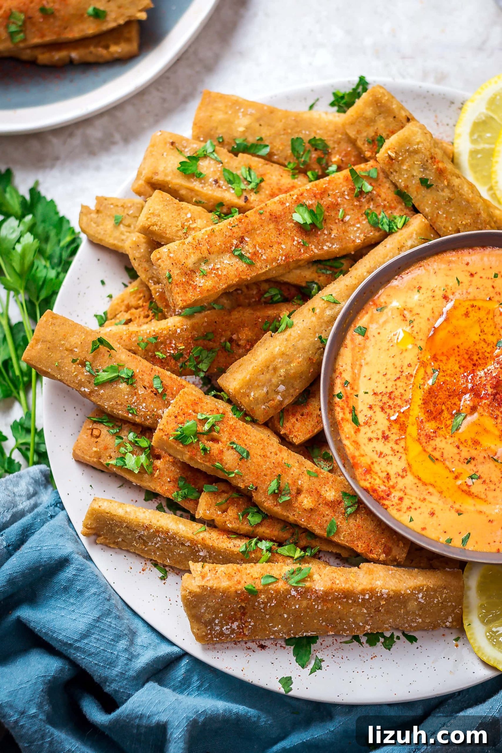 Hummus Fries with Spicy Tahini Dipping Sauce 4 A close up of Hummus Fries with Spicy Tahini Dip on a round white plate with a blue cloth below.