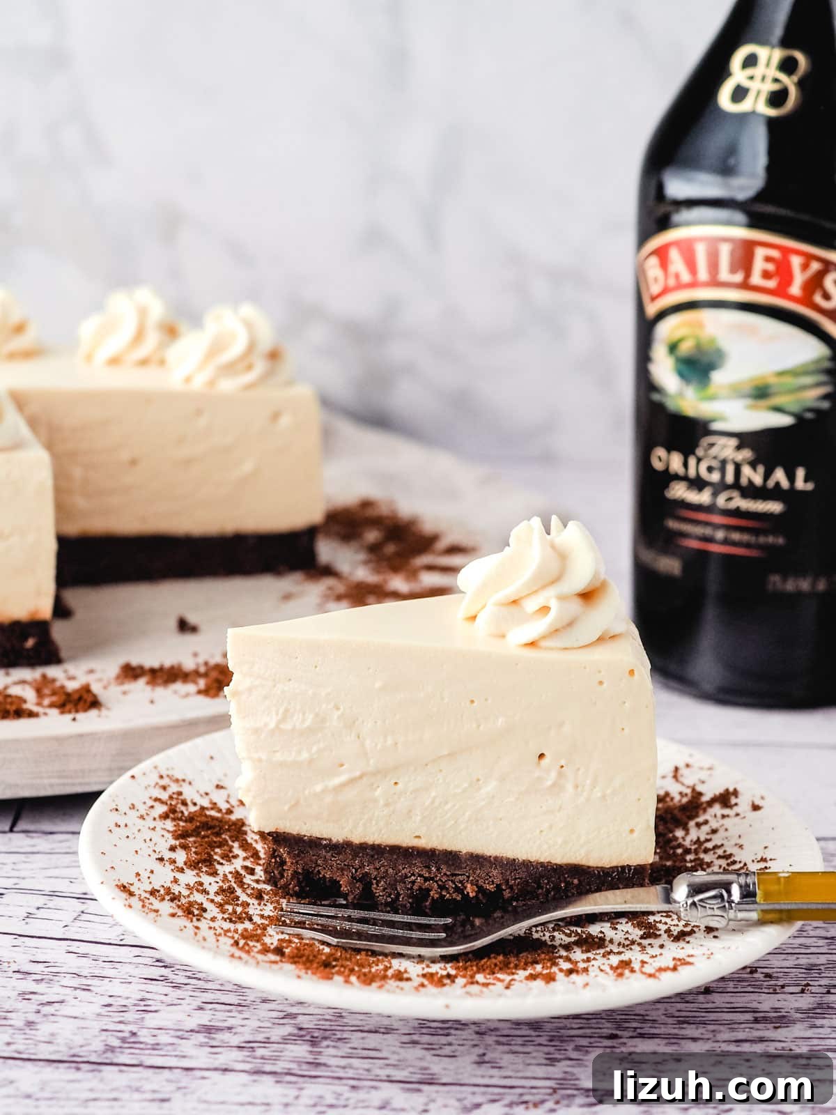No-Bake Baileys Cheesecake Recipe: Creamy Irish Cream Dessert 12 Baileys cheesecake on a plate with cheesecake and Baileys in the background.