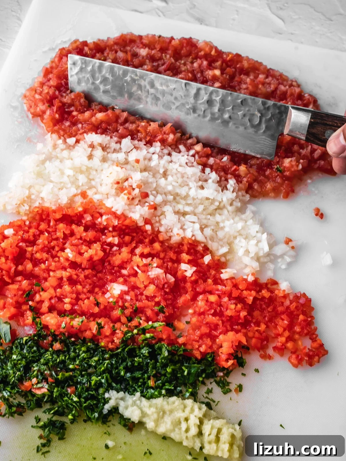 Chopping board with very finely chopped tomatoes, onion, bell pepper, parsley and garlic.