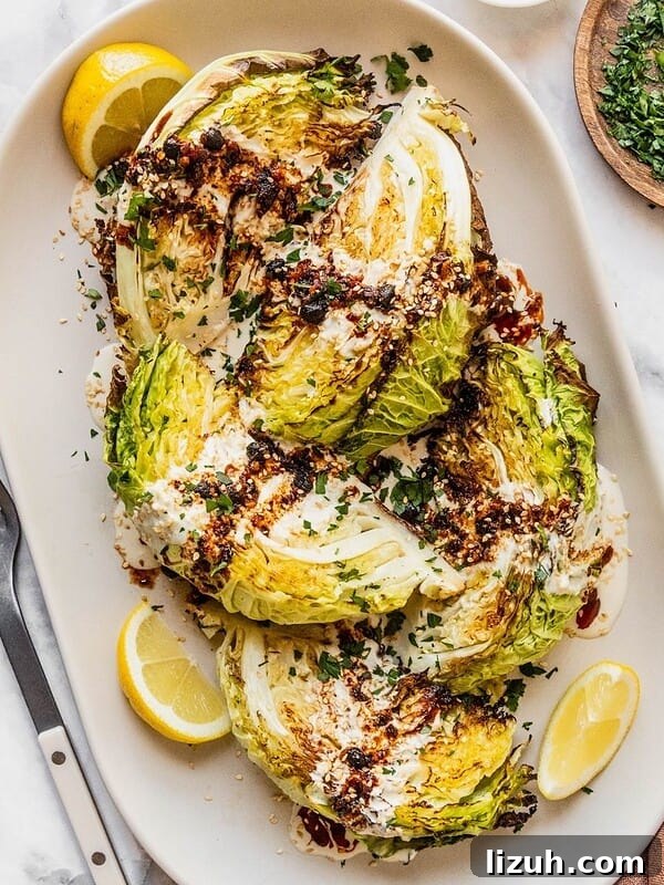Roasted cabbage wedges with tahini and chili crisp drizzle on a serving platter garnished with parsley and lemon slices.