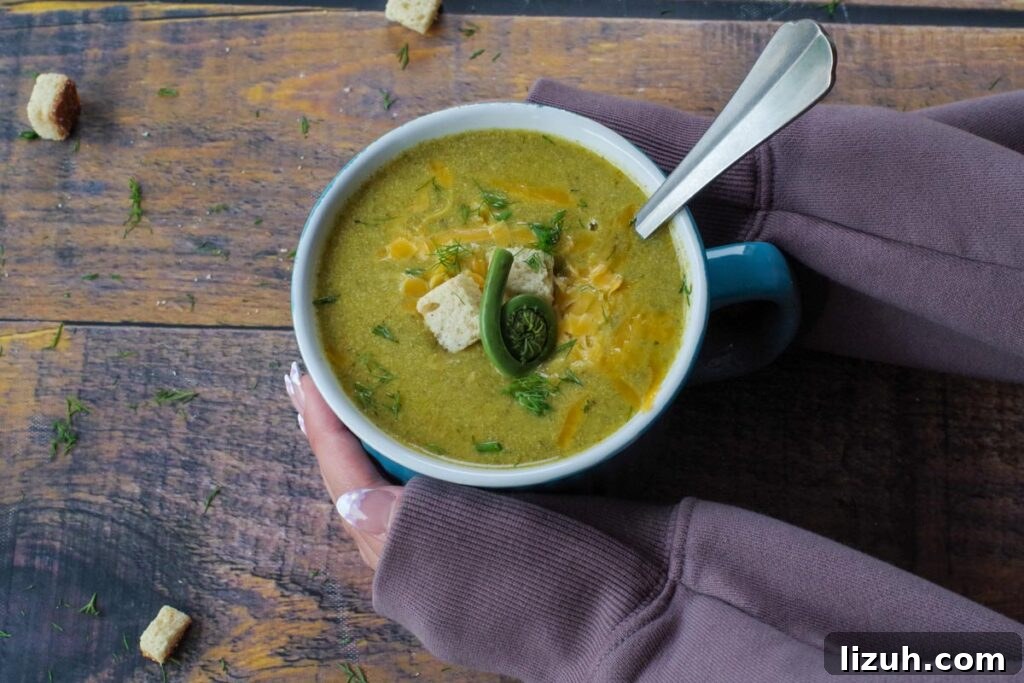 Creamy Fiddlehead and Cheese Soup Recipe 2 fiddlehead soup in a mug with a spoon in it and hands cradling it
