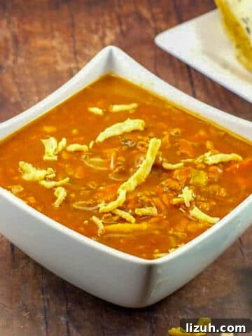 Carrot Tomato Soup in white bowl on brown wooden surface, with bread in background