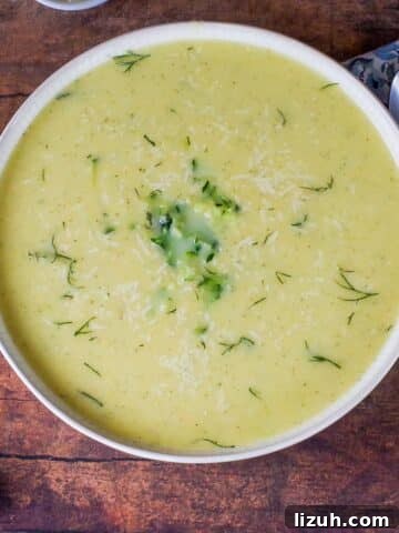 Zucchini Potato soup in a beige bowl with blue paisley napkin and spoon on the side
