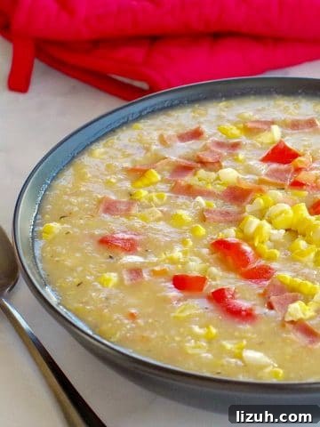 Healthy Corn Chowder in a black bowl, with a spoon on the side and red over mitts in background