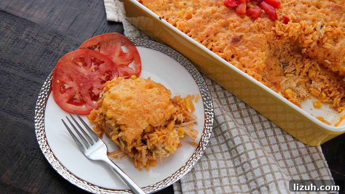 Imperial Rice: Creamy Baked Rice with Chicken and Shrimp 5 a serving of yellow rice, shredded chicken, cheese, and two tomato slices on a white plate with a fork. A yellow casserole dish in the background.