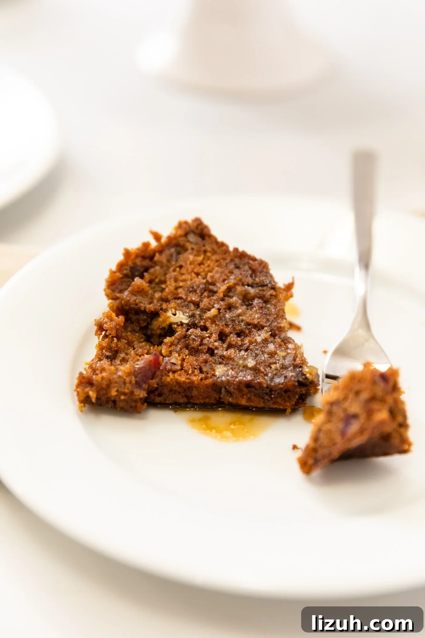 Sticky Date Pudding Cake Recipe with Caramel Sauce 5 Piece of date pecan cake sitting on white plate with fork holding piece all on white surface