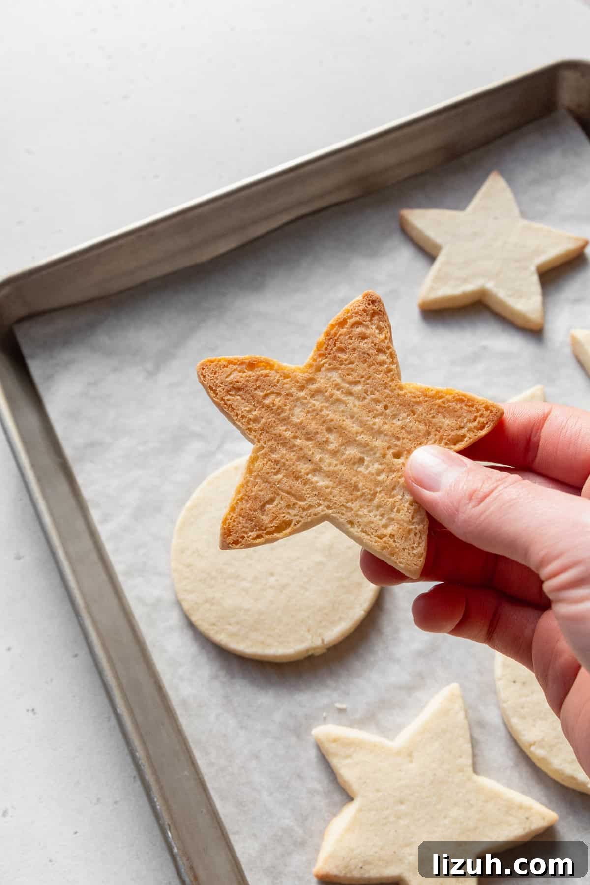 Gluten-Free Sugar Cookie Recipe for Crisp, Chewy Cookies 11 A hand holding a star-shaped sugar cookie, showing the golden color of the bottom of the cookie.
