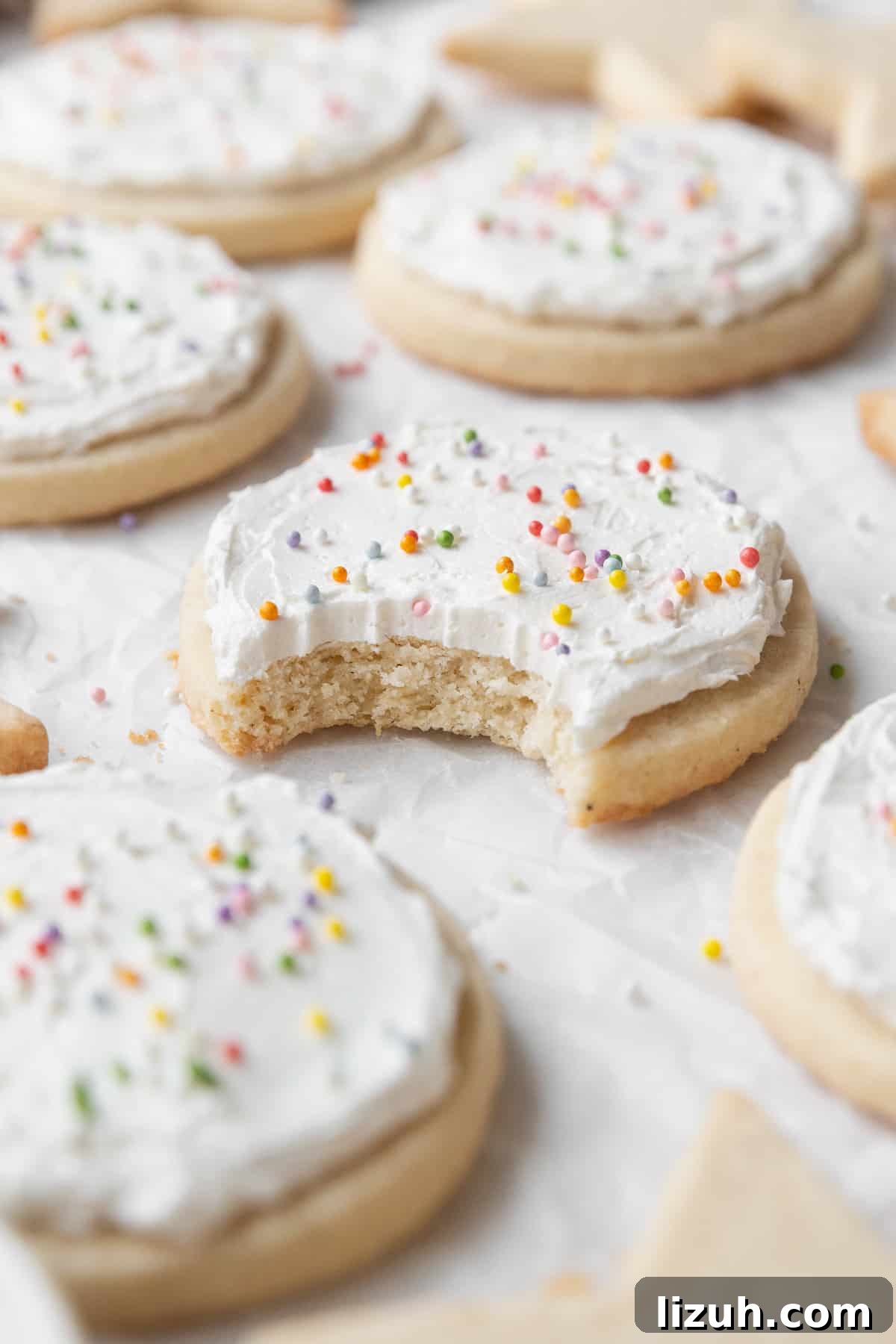 Gluten-Free Sugar Cookie Recipe for Crisp, Chewy Cookies 14 A bitten frosted gluten-free sugar cookie with sprinkles surrounded by more cookies.