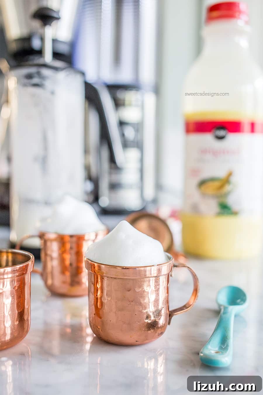 Eggnog Espresso Shooters: Holiday Coffee Cocktail Recipe 3 copper small mug with milk foam on it, eggnog in the background