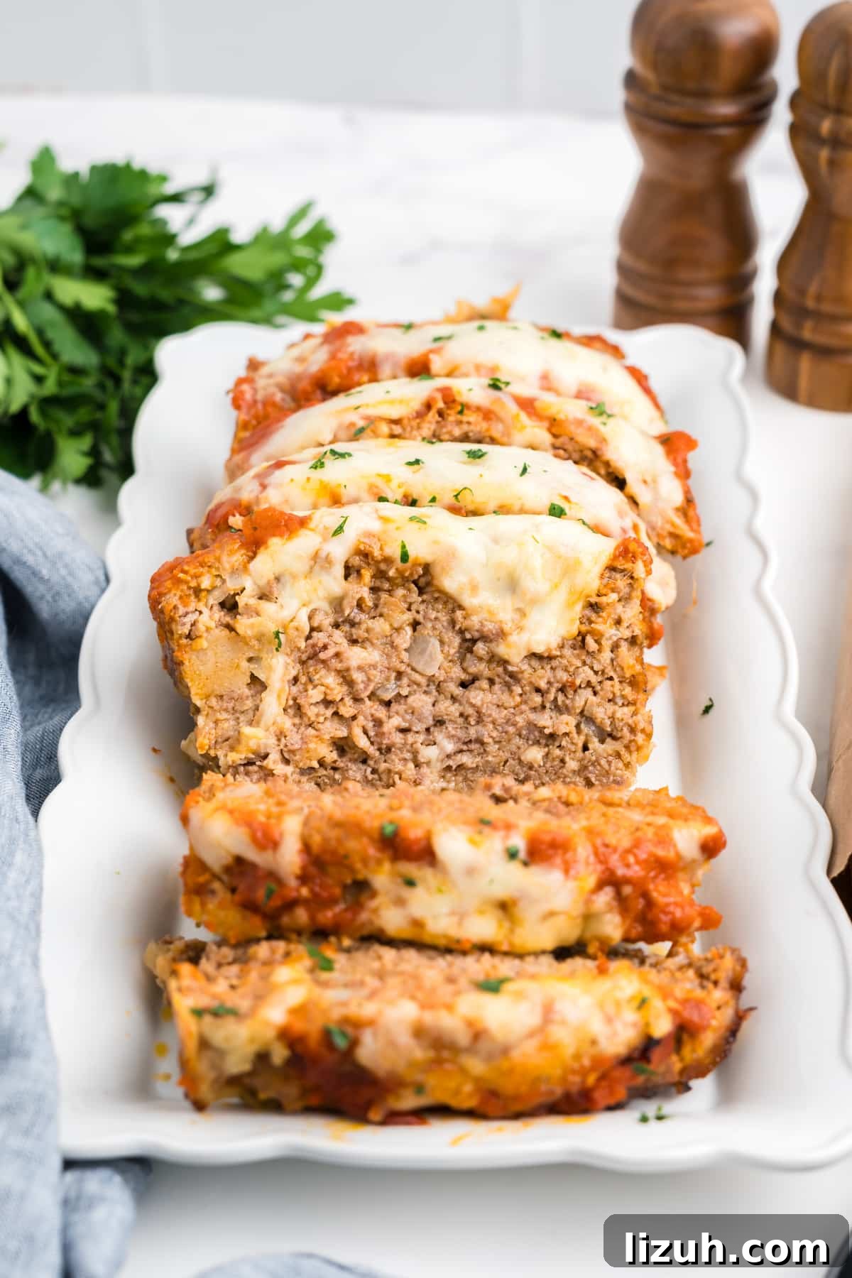 Italian meatloaf with cheese on top sliced on a white platter. 