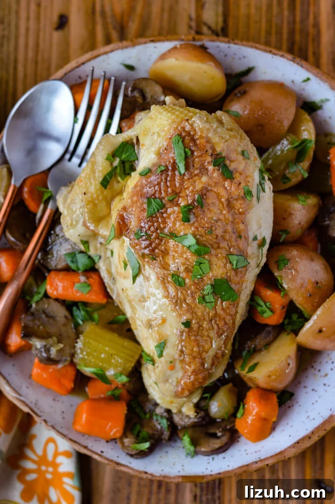 A cooked chicken breast on a bed of cooked carrots, potatoes and celery with a spoon and fork.