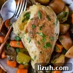 A cooked chicken breast on a bed of cooked carrots, potatoes and celery with a spoon and fork.