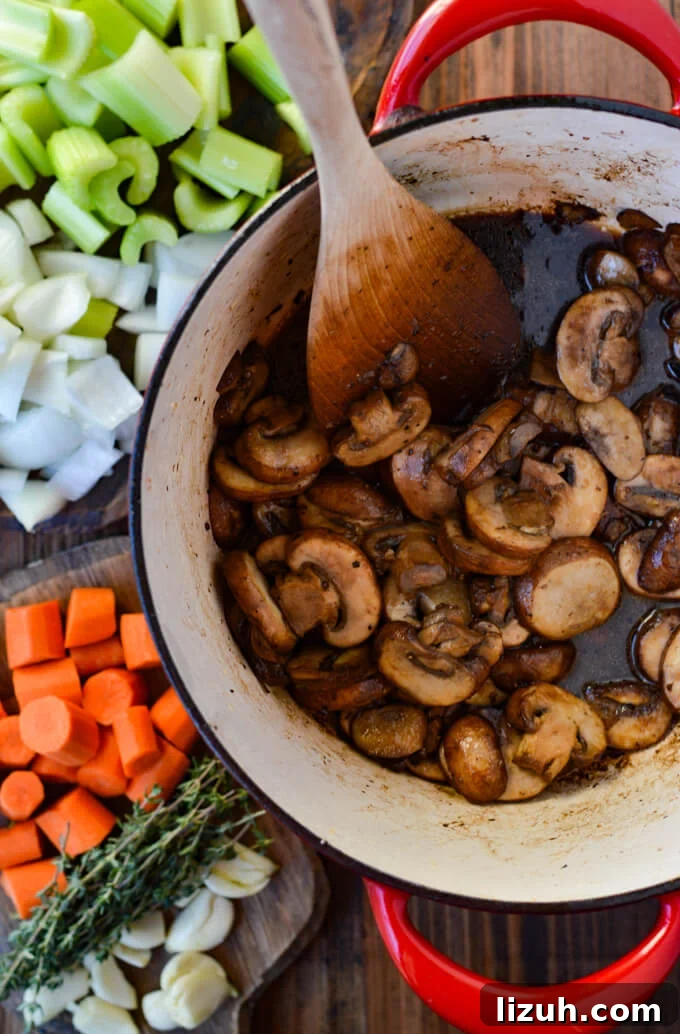 Sliced mushrooms cooking in a dutch oven with celery, onions, carrots and thyme on the side.