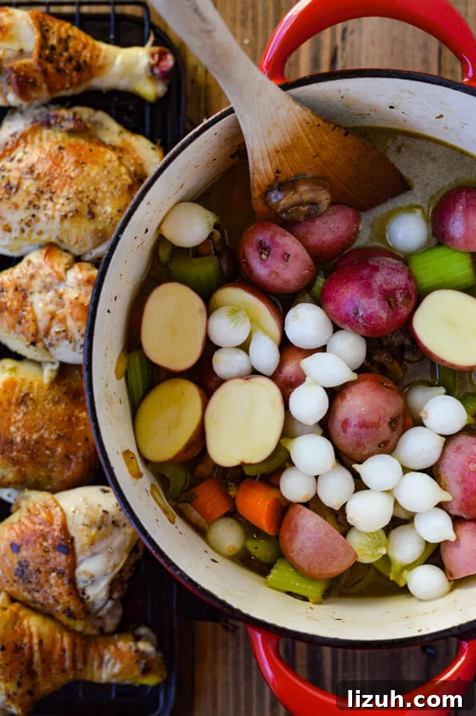 A dutch oven with cooked onions, carrots, celery and raw red potatoes and frozen pearl onions.