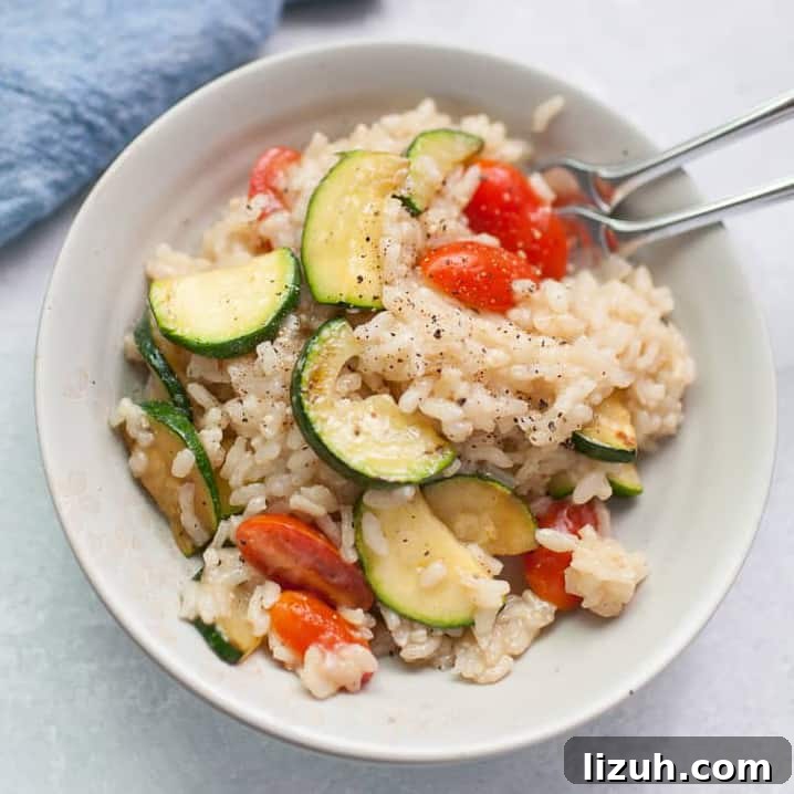 A bowl of creamy risotto mixed with sliced zucchini and cherry tomatoes, topped with ground black pepper-perfect for anyone learning how to cook risotto, with two forks resting in the bowl.