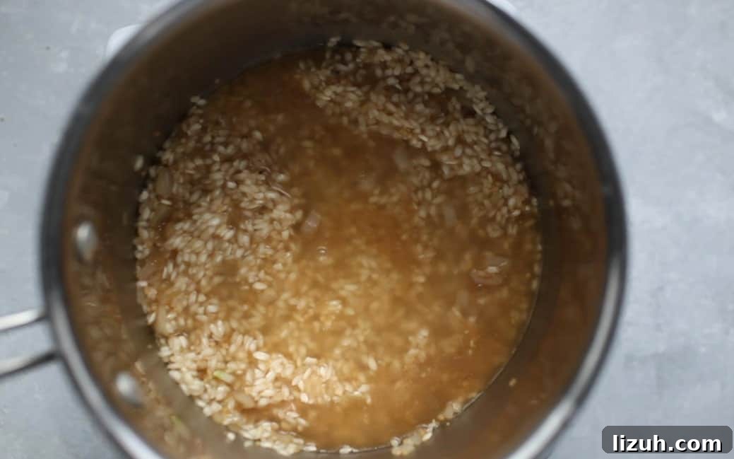 A pot filled with chicken brother, risotto rice and a wooden spoon.