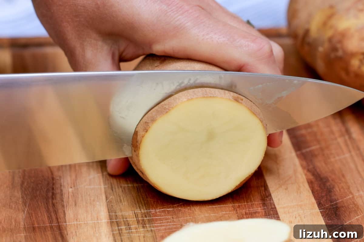 Crispy Grilled Sliced Potatoes Recipe for Summer BBQs 4 Slicing a russet potato with large knife into ¼" pieces on wooden cutting board.