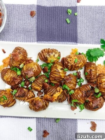 Smoked hasselback potatoes topped with cheese, bacon, and green onions on white dish
