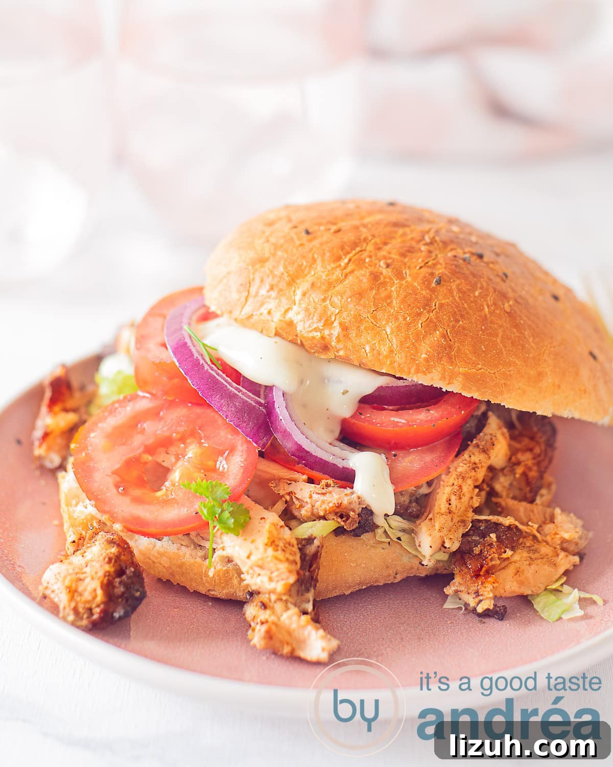 An elevation photo with a Turkish sandwich topped with chicken döner, tomato, lettuce and garlic sauce. A white background. A pink white tea towel in the background.
