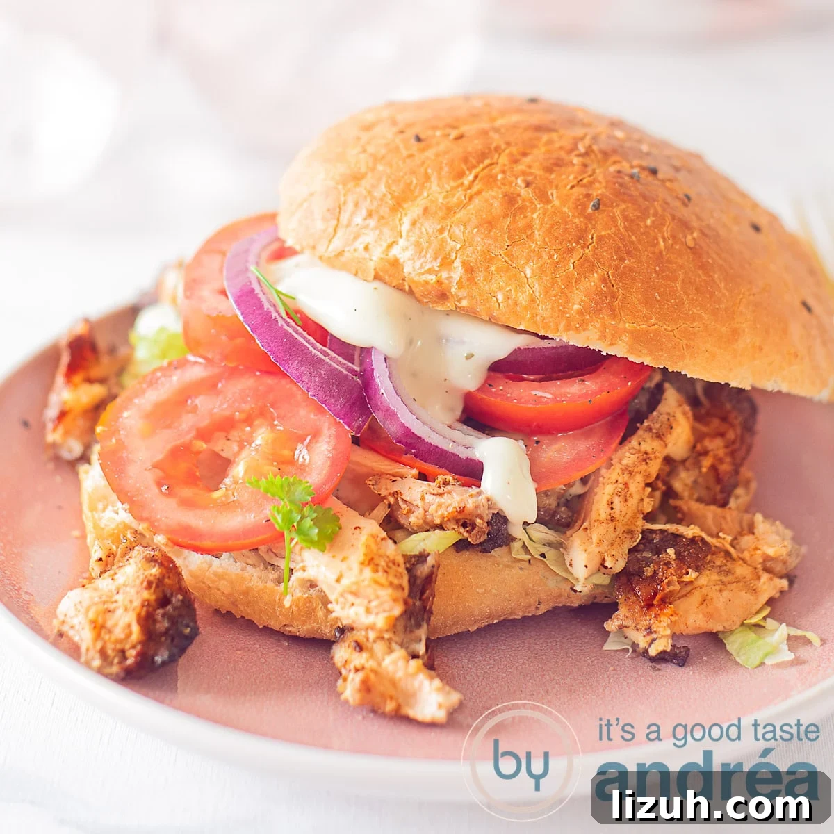 A Turkish sandwich with Döner chicken, tomato and lettuce and garlic sauce. A pink plate and a white background.