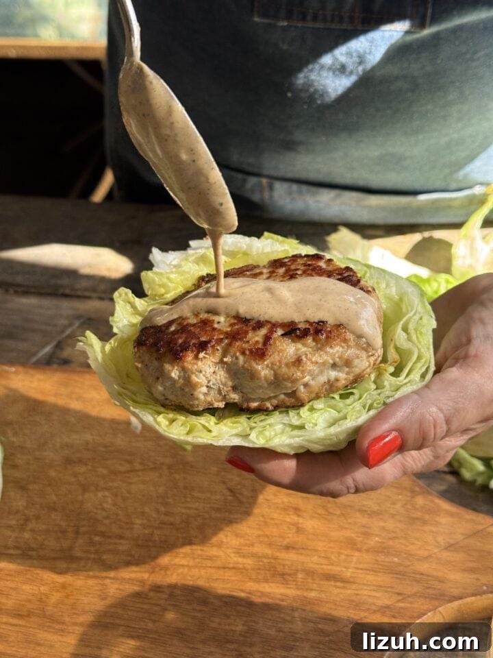 Quick Weeknight Ground Chicken Burgers Recipe 9 a photo drizzling sauce on a ground chicken burger on a lettuce bun