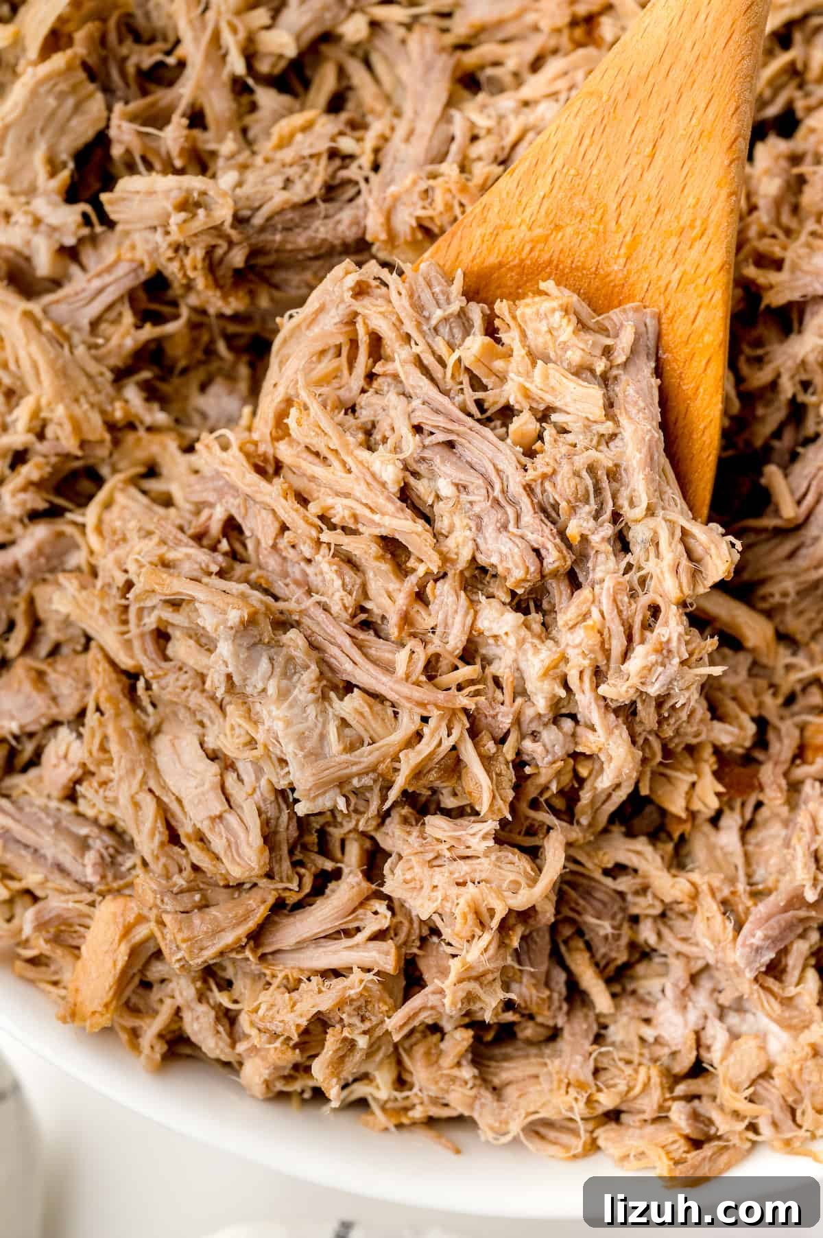 Shredded pulled pork on a large wooden spoon.