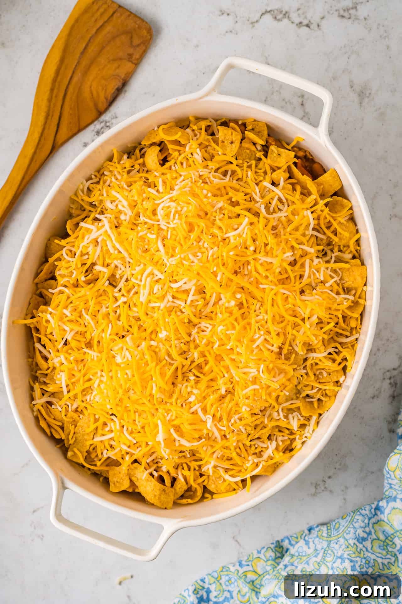 Seasoned ground beef with tomatoes and beans topped with corn chips and cheese in a casserole dish.