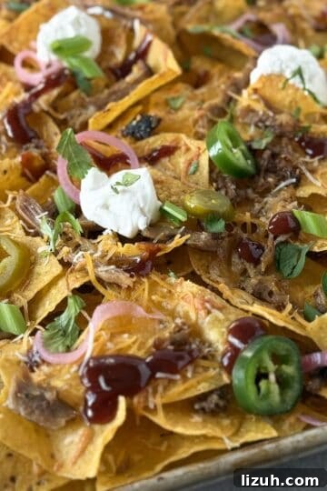 Close-up of leftover BBQ pulled pork nachos with melted cheese, barbecue sauce, pickled red onions, jalapeños, and sour cream.