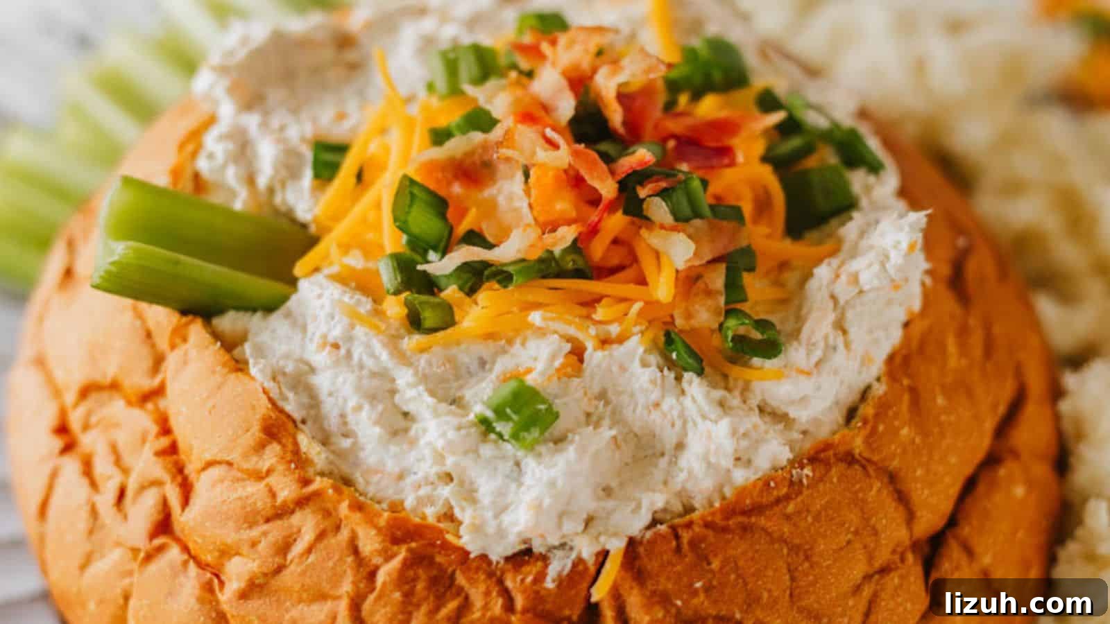 35 Game-Day Recipes to Win Your Season’s Food Lineup 18 A bread bowl filled with a creamy dip, garnished with shredded cheese, chopped green onions, and bacon bits. Celery sticks are placed on the side.