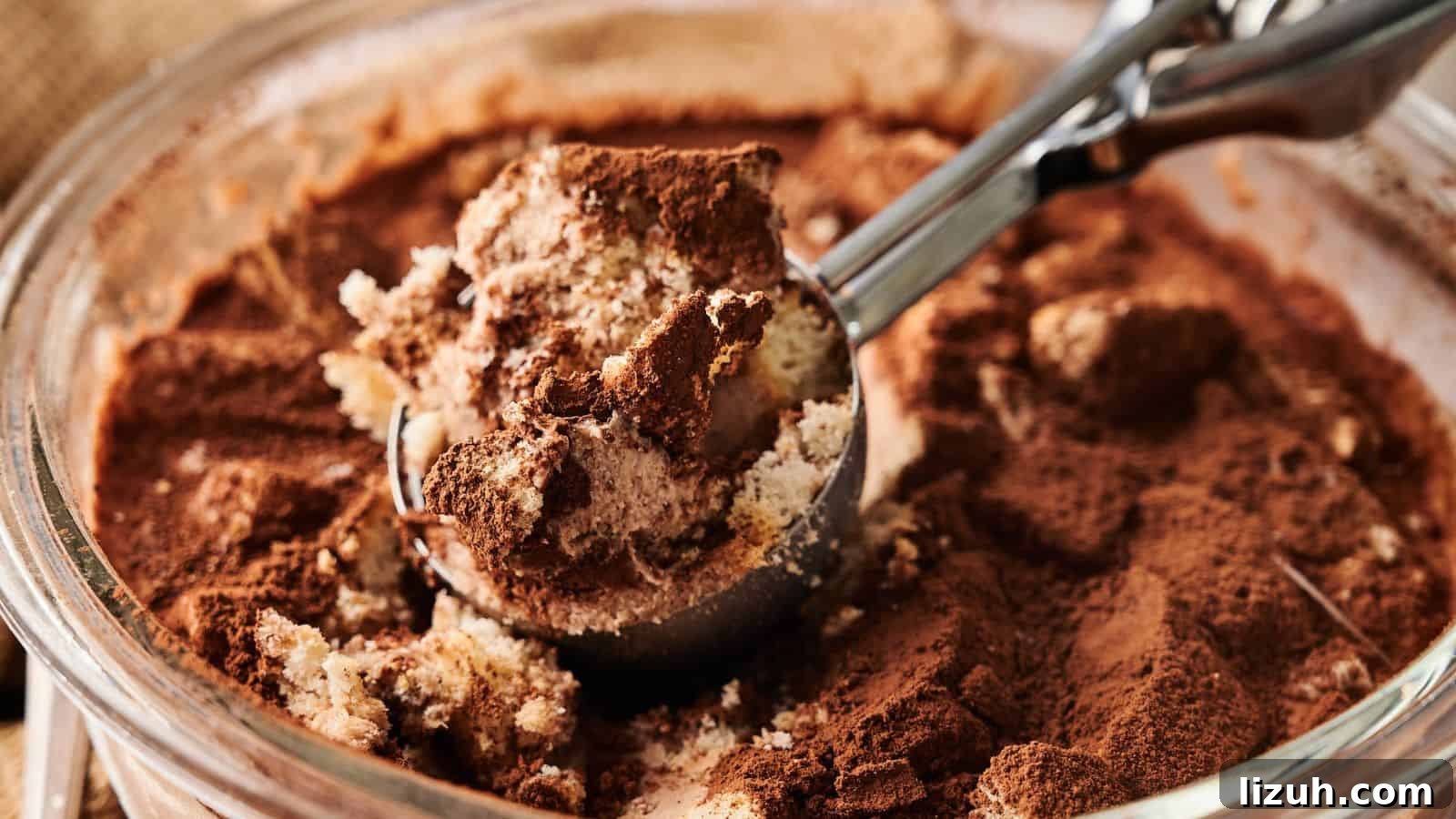 35 Game-Day Recipes to Win Your Season’s Food Lineup 32 A close-up of a glass dish with tiramisu being scooped out, showing layers of cream, cake, and cocoa powder.