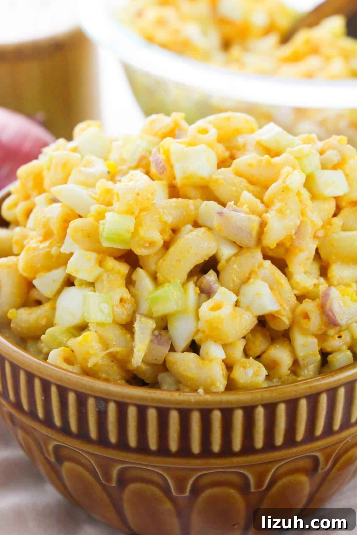 A brown bowl filled with a side featuring chopped eggs, celery, and possibly red onion, all tossed in a creamy dressing.